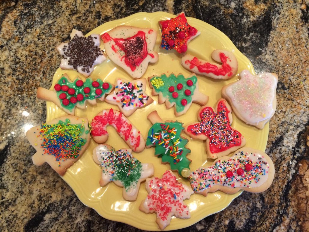 A yellow plate of decorated Christmas cookies on a stone countertop