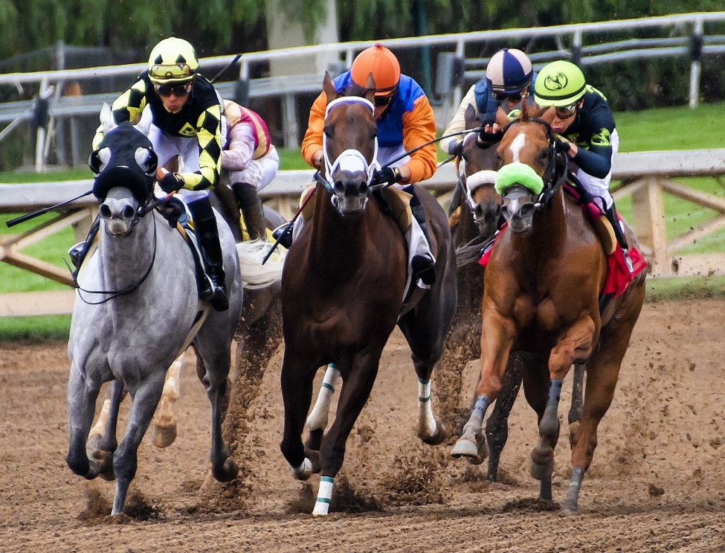 A group of five horses with jockeys racing on a dirt track