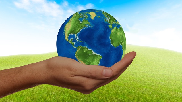 A hand holding the globe over green grass and blue, cloudy sky